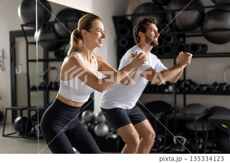 Two young people exercising in the gym in squatting position 135334123