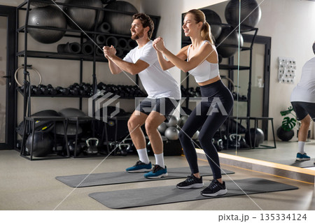 Two young people exercising in the gym in squatting position 135334124