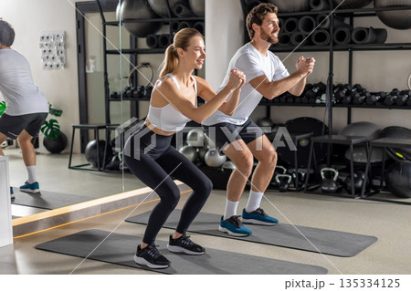 Two young people exercising in the gym in squatting position Two young people exercising in the gym in squatting position 135334125