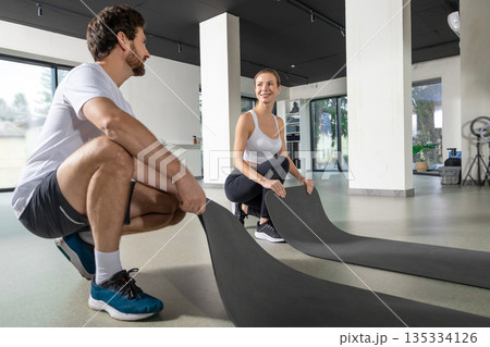 Young man and woman preparing mats for the workout in the gym Young man and woman preparing mats for the workout in the gym 135334126