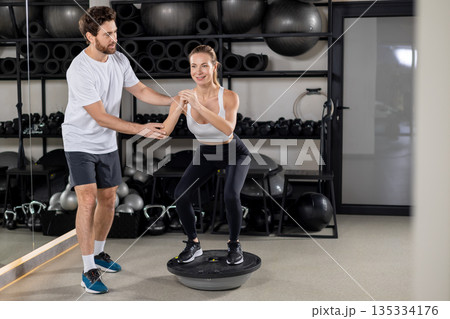 Blonde young woman exercising in the gym with a coach Blonde young woman exercising in the gym with a coach 135334176