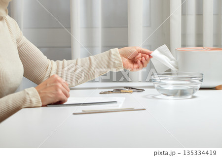 Woman's hand pulling a white tissue from a dispenser for hand hygiene 135334419