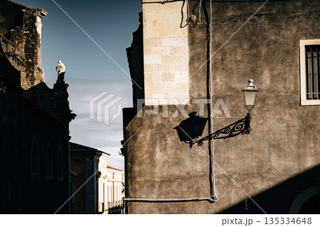 Light And Shadow On Catania Street Wall: Italian Sicilian Urban Scene With Weathered Facade, Window, And Street Lamp In Strong Sunlight Light And Shadow On Catania Street Wall: Italian Sicilian Urban Scene With Weathered Facade, Window, And Street Lamp In Strong Sunlight 135334648