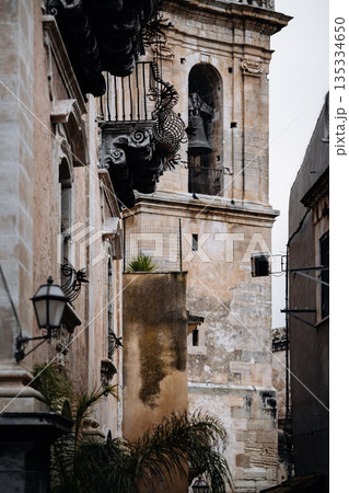 Historic Urban Architecture In Ragusa, Sicily: Weathered Stone Buildings, Narrow Streets, Layered Rooftops, And Church Dome Forming Dense Mediterranean Cityscape 135334650