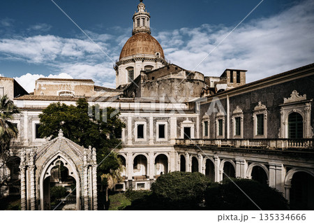 Benedictine Monastery Of San Nicolo Arena In Catania, Sicily: Historic Baroque Courtyard With Arched Walkways, Stone Facades, And Domed Church Structure Benedictine Monastery Of San Nicolo Arena In Catania, Sicily: Historic Baroque Courtyard With Arched Walkways, Stone Facades, And Domed Church Structure 135334666
