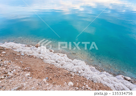 Sand covered with crystalline salt on shore of Dead Sea, turquoise blue water near - typical scenery at Ein Bokek beach, Israel 135334756