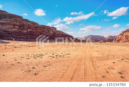 Rocky massifs on red sand desert, bright cloudy sky in background, small 4wd vehicle and camel at distance - typical scenery in Wadi Rum, Jordan 135334760