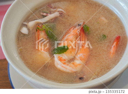 top view Seafood tom yum with clear soup in a ceramic cup on a galvanized plate on table background, food, eat, object, copy space 135335172