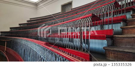 A view of empty, multi-tiered, antique wooden classroom seats with decorative railings in a historic interior. Educational system concept, timeless design. A view of empty, multi-tiered, antique wooden classroom seats with decorative railings in a historic interior. Educational system concept, timeless design. 135335326