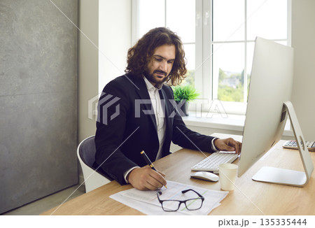 Business man working at office on a pc computer sitting at the desk on workplace. Business man working at office on a pc computer sitting at the desk on workplace. 135335444