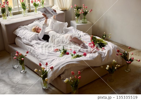 Calm cozy reading, Tranquil person lounging with book amidst soft floral decorations and simple decor 135335519