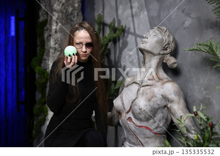 Woman gestures with bright green sphere near ancient stone statue Woman gestures with bright green sphere near ancient stone statue 135335532