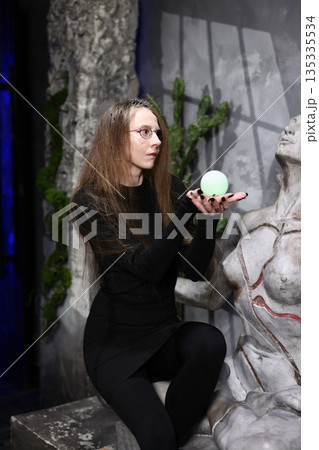 Woman with piercing gaze cradles glowing orb in abandoned city scene 135335534