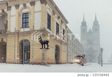 Historic Altermarkt square Magdeburg at heavy snowfall show Rathaus architecture, statues lanterns empty urban space winter storm. Municipal service tractor cleaning snow with snow plow 135336483