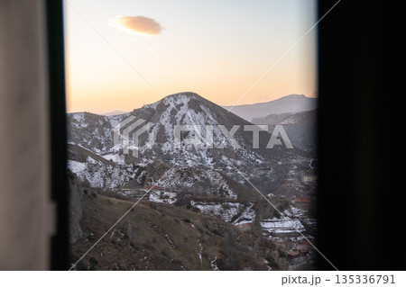 Mountain landscape of Goris, Armenia at dawn, seen through a window with sheer curtains, soft light, muted colors, and a calm morning atmosphere 135336791