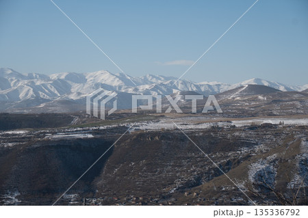 Snow-covered mountain range in Armenia stretches across rolling hills, deep valleys under clear blue sky, with cool tones, quiet winter atmosphere Snow-covered mountain range in Armenia stretches across rolling hills, deep valleys under clear blue sky, with cool tones, quiet winter atmosphere 135336792