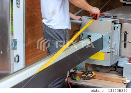 Gutter worker measures long metal rain gutter system with ruler while working inside Gutter worker measures long metal rain gutter system with ruler while working inside 135336853