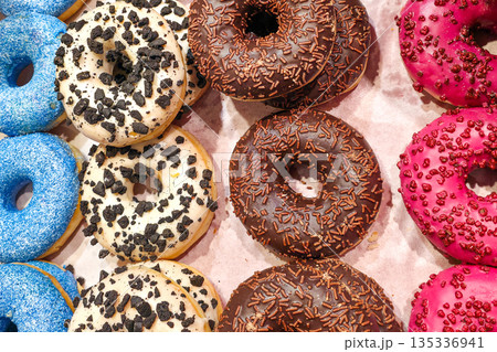 Colorful assortment of glazed donuts with sprinkles and cookie crumbs in bakery display 135336941