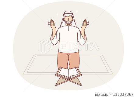 Muslim man prays on knees in front koran, observing islamic ritual during holy month of ramadan Muslim man prays on knees in front koran, observing islamic ritual during holy month of ramadan 135337367