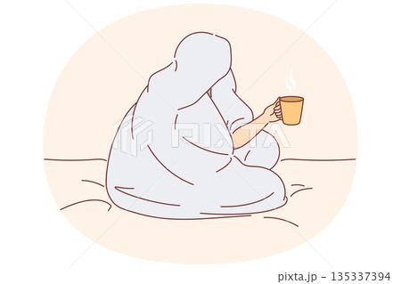 Man drinks coffee sitting on bed and wrapped in blanket to warm up after walk along winter street 135337394