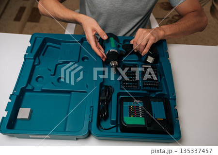 Cropped shot of skilled handyman showing cordless power drill, battery charger and many assorted screwdriver bits inside sturdy turquoise tool case, ready for home improvement or construction work. Cropped shot of skilled handyman showing cordless power drill, battery charger and many assorted screwdriver bits inside sturdy turquoise tool case, ready for home improvement or construction work. 135337457