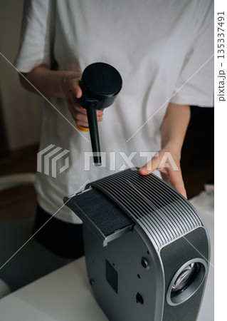 Vertical shot of person cleaning home cinema projector with air blower, providing regular maintenance for electronic device performance and longevity, keeping technology efficient. Vertical shot of person cleaning home cinema projector with air blower, providing regular maintenance for electronic device performance and longevity, keeping technology efficient. 135337491