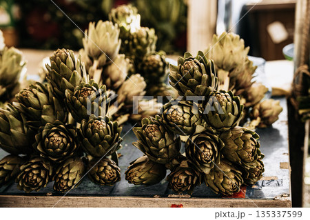 Fresh Green Artichokes At Market Stall: Raw Seasonal Vegetables With Leaves And Stems Displayed In Natural Organic Arrangement Fresh Green Artichokes At Market Stall: Raw Seasonal Vegetables With Leaves And Stems Displayed In Natural Organic Arrangement 135337599