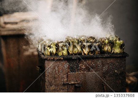 Fresh Artichokes Barbecue At Catania Market In Sicily: Trimming And Steaming Green Vegetables On Hot Surface In Traditional Street Food Scene Fresh Artichokes Barbecue At Catania Market In Sicily: Trimming And Steaming Green Vegetables On Hot Surface In Traditional Street Food Scene 135337608