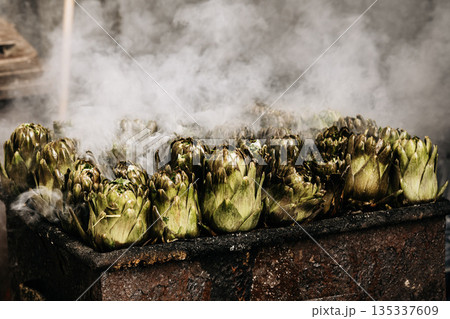 Fresh Artichokes Barbecue At Catania Market In Sicily: Trimming And Steaming Green Vegetables On Hot Surface In Traditional Street Food Scene 135337609
