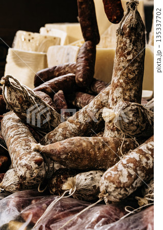 Traditional Cured Sausages At Market Stall: Rustic Dry Meat Products Displayed In Abundant Arrangement With Natural Texture And Warm Light Traditional Cured Sausages At Market Stall: Rustic Dry Meat Products Displayed In Abundant Arrangement With Natural Texture And Warm Light 135337702