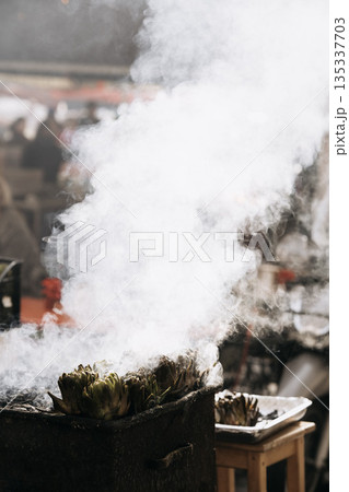 Fresh Artichokes Barbecue At Catania Market In Sicily: Trimming And Steaming Green Vegetables On Hot Surface In Traditional Street Food Scene 135337703