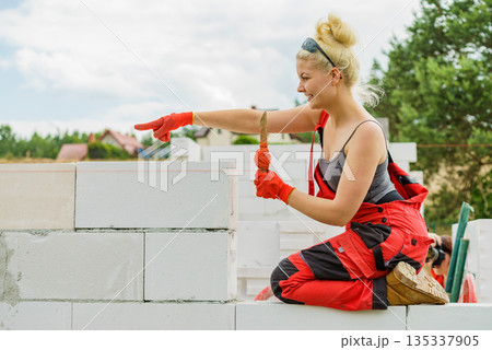 Woman using string as level in wall construction. Woman using string as level in wall construction. 135337905
