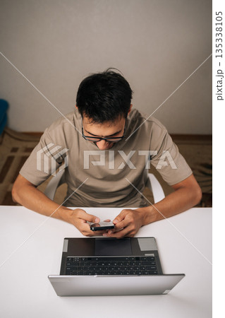 Focused bearded businessman working late at night in home office, using smartphone and laptop to manage business tasks and meet deadlines with focused concentration and professionalism 135338105