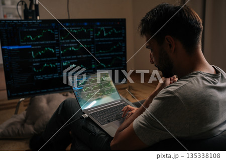 Pensive focused trader male engrossed in financial analysis and day trading, using laptop and large external monitor displaying various stock market and cryptocurrency charts from home office. Pensive focused trader male engrossed in financial analysis and day trading, using laptop and large external monitor displaying various stock market and cryptocurrency charts from home office. 135338108
