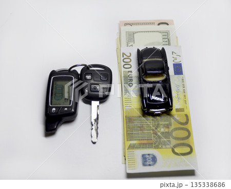 Car keys with a key fob, euro banknotes, and a model car on a white background Car keys with a key fob, euro banknotes, and a model car on a white background 135338686