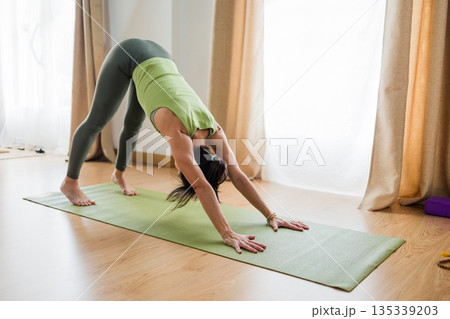 Hispanic woman performing downward facing dog yoga pose, adho mukha svanasana 135339203