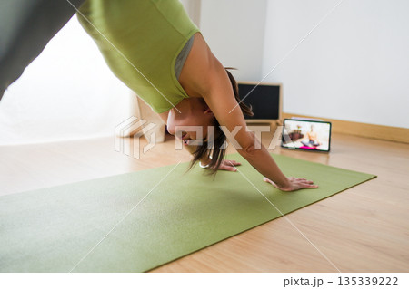 Hispanic woman practicing online yoga surya namaskar at home Hispanic woman practicing online yoga surya namaskar at home 135339222