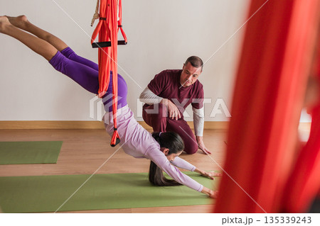 Woman doing aerial yoga with instructor guiding Woman doing aerial yoga with instructor guiding 135339243