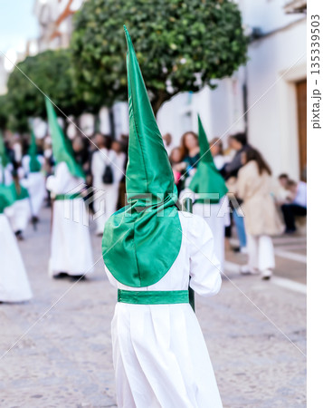 Nazarene walking in a holy week procession in Andalusia Spain holding a silver cross. 135339503