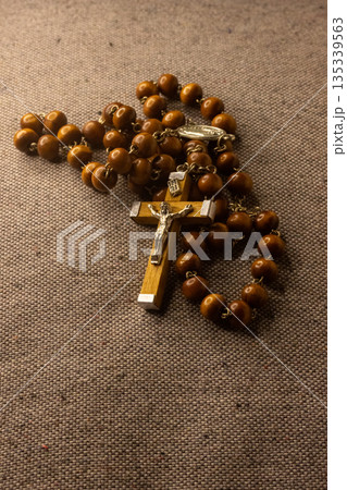 Wooden rosary with a metal crucifix featuring Jesus Christ's figure is resting on textured fabric Wooden rosary with a metal crucifix featuring Jesus Christ's figure is resting on textured fabric 135339563