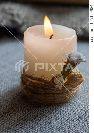 Candle glowing with a bright flame wrapped with natural jute on grey background 135339984
