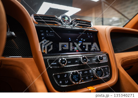 Close up of Bentley Bentayga Speed center console, navigation on screen, Breitling style analog clock, chrome vents, knurled controls, tan leather, studio lighting. 135340271