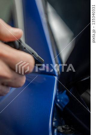A technician moves a heat pen along a panel gap on a glossy blue luxury car in a dealership service bay. Soft lighting reveals precise detailing and a metallic finish. 135340331