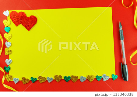 Blank yellow card mockup on red background with colorful glitter hearts and pen. 135340339