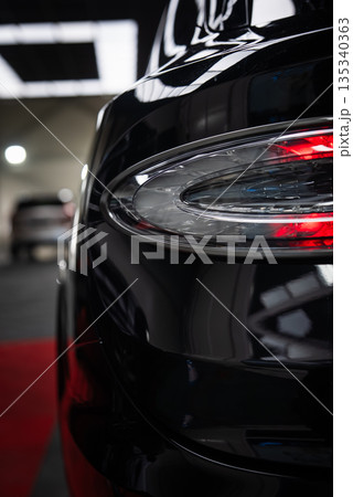 Glossy black Bentley Bentayga Speed indoors, rear three quarter view. Oval LED taillight shows red illumination, soft panels overhead, blurred car in background. Glossy black Bentley Bentayga Speed indoors, rear three quarter view. Oval LED taillight shows red illumination, soft panels overhead, blurred car in background. 135340363