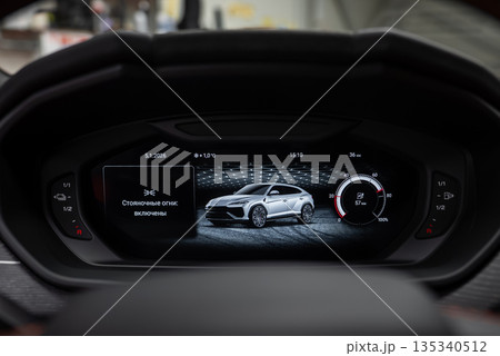 Close up instrument cluster shows Urus SE render, Russian menu text, and a circular tachometer gauge, with date, temperature, time, and settings in a workshop setting. 135340512