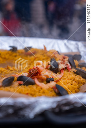 A steaming pan of seafood paella with mussels and shrimp is cooked and served at a Christmas market in Riga, Latvia, with soft winter light and drifting steam. 135340557