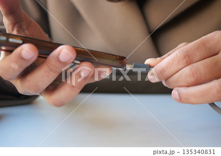 Person connects charger to mobile phone at a table 135340831