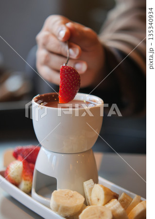 Dipping fruit in chocolate at a dessert cafe in the evening Dipping fruit in chocolate at a dessert cafe in the evening 135340934