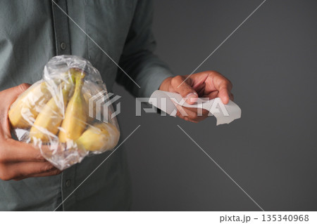 Person holding plastic bag with bananas and shopping receipt in hand Person holding plastic bag with bananas and shopping receipt in hand 135340968